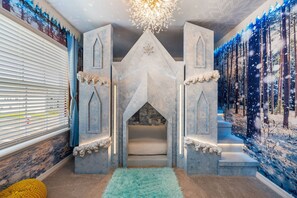 Ein Zimmer mit einem Spielbereich im Burgstil, inklusive Treppe und einer Wandmalerei von einem verschneiten Wald.