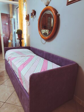 A room with a purple sofa bed, a wooden-framed mirror, and a potted plant. - A villa with a view of the sea, surrounded by nature, tranquility, and relaxation in the heart of Sicily. (Santo Stefano)