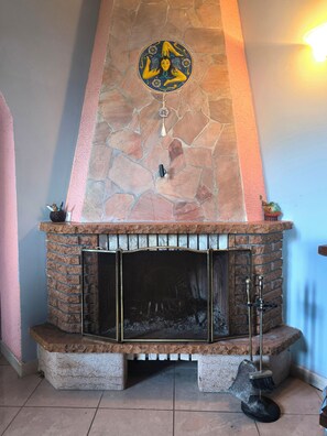 Una chimenea de piedra con un emblema decorativo encima, una puerta mosquitera de metal y una escoba en el suelo.