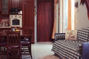 A cozy living room with a checkered sofa, a dining table with chairs, and a kitchen area with wooden cabinets and a vintage oven. - A villa with a view of the sea, surrounded by nature, tranquility, and relaxation in the heart of Sicily. (Santo Stefano)