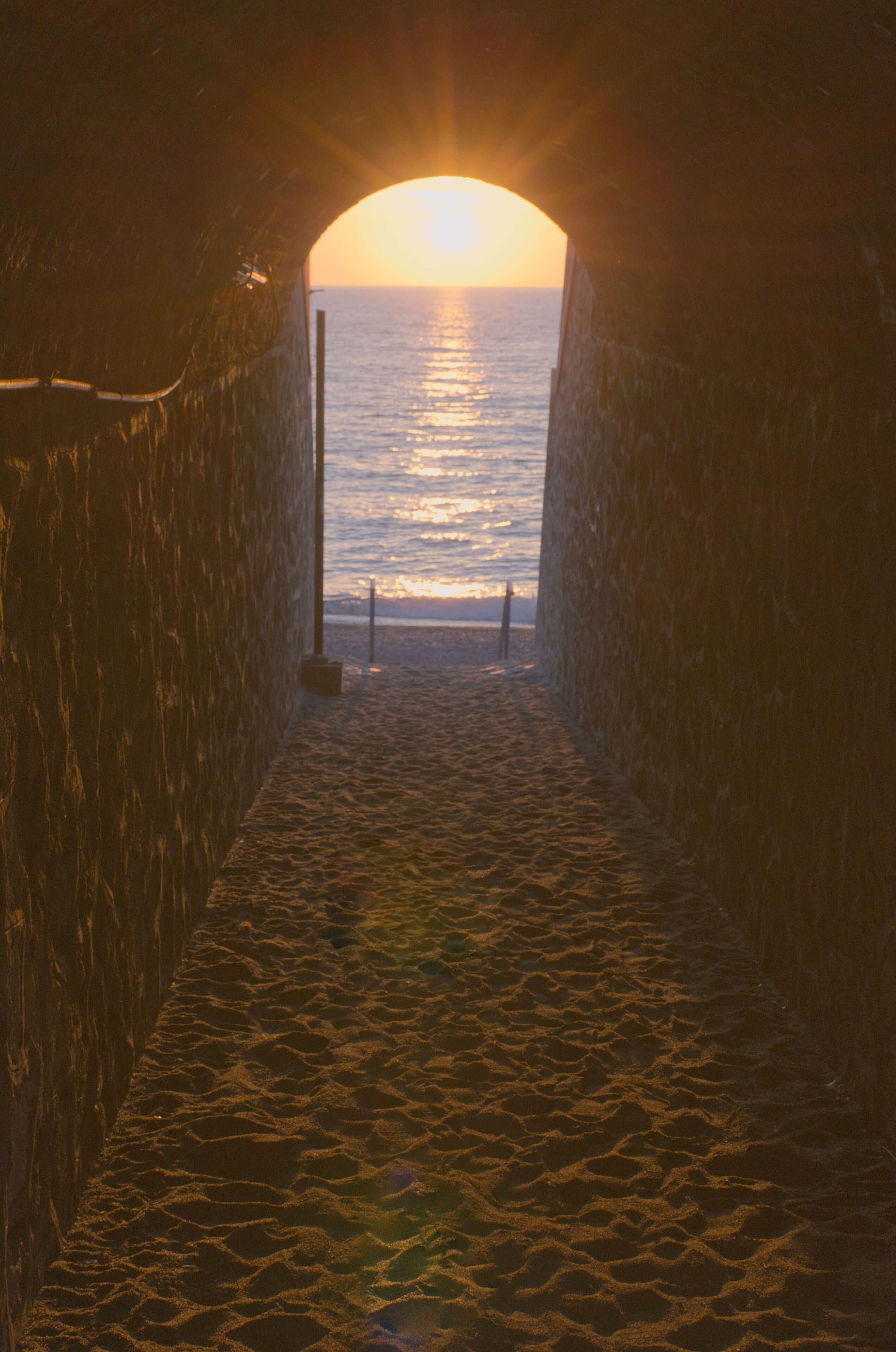 Un tunnel qui mène à une plage offrant une vue sur le coucher de soleil.