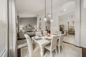 A dining area with a white table set for four, surrounded by chairs, in a room with a modern design and a visible kitchen area in the background. - 4036 Oakrise Loop (Davenport)