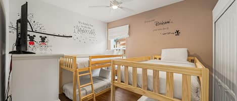 A room with bunk beds, a ceiling fan, a wall with Disney-themed decals, and a window with a view.