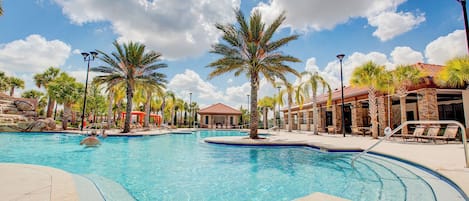 A large outdoor swimming pool with palm trees, lounge chairs, and a covered area with a red roof.