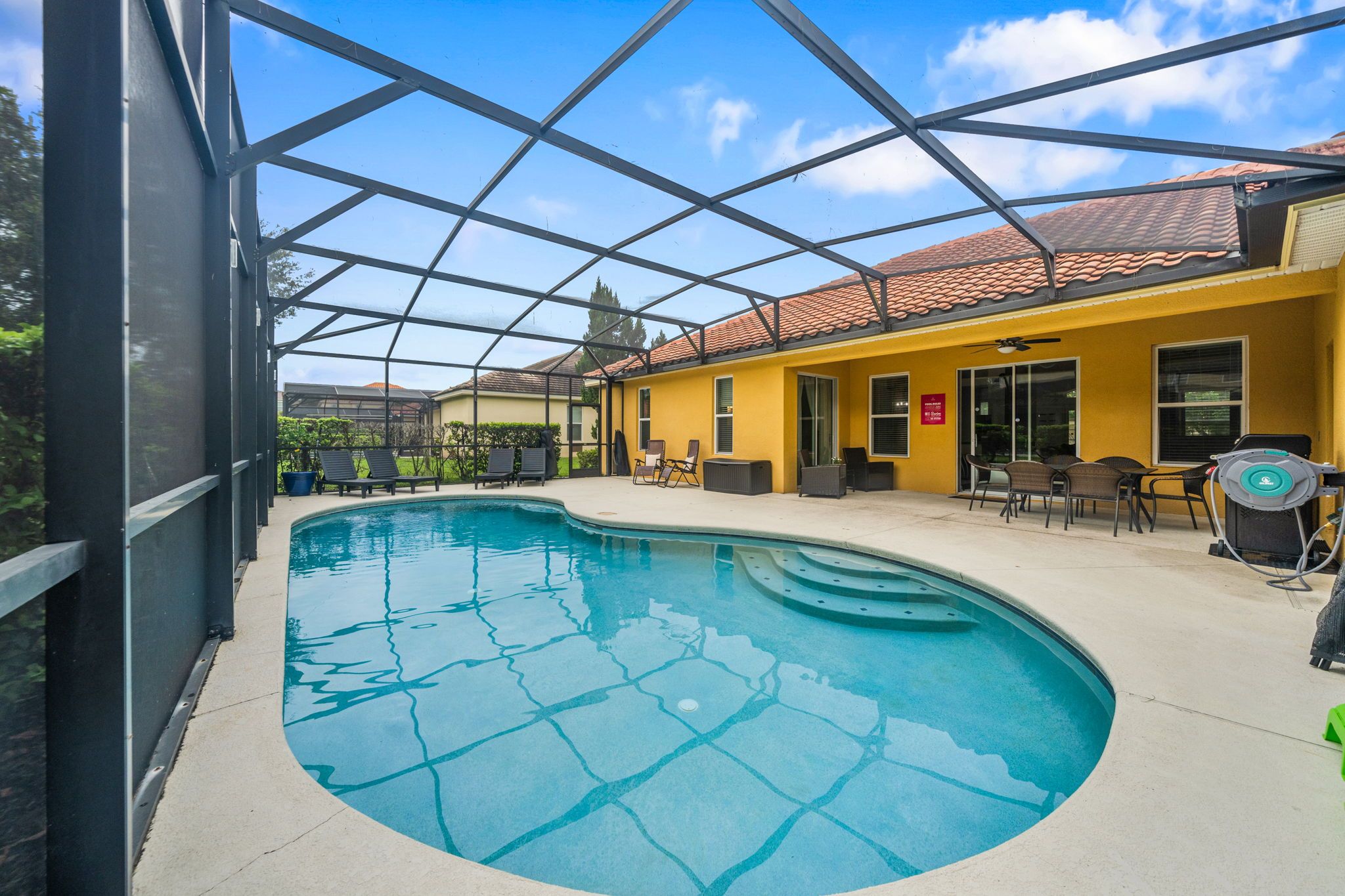 Une piscine intérieure dotée d’un toit en verre, entourée de chaises longues et bordée d’un bâtiment jaune au toit recouvert de tuiles.