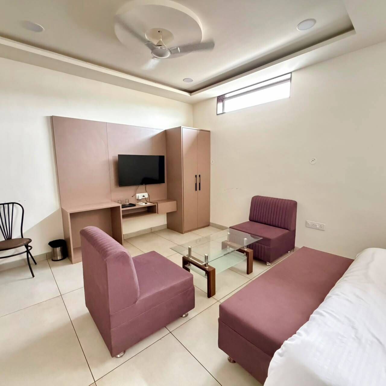 Una habitación de hotel moderna con sofá, una mesa de centro de vidrio, un televisor montado en la pared y un ventilador de techo.