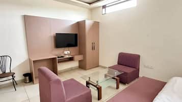 Una habitación de hotel moderna con sofá, una mesa de centro de vidrio, un televisor montado en la pared y un ventilador de techo.