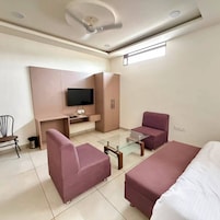 Una habitación de hotel moderna con sofá, una mesa de centro de vidrio, un televisor montado en la pared y un ventilador de techo.