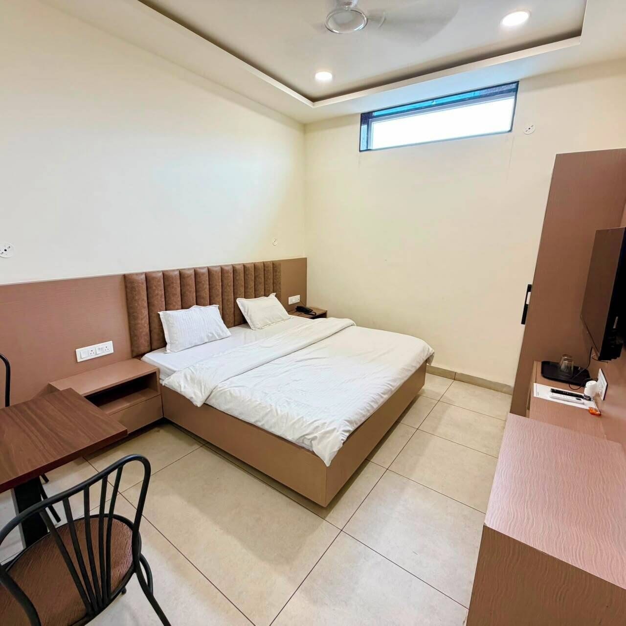 A hotel room with a bed, a desk, a chair, a television, and a window.