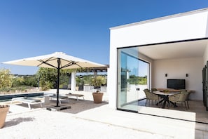 A modern outdoor patio with a pool, lounge chairs, and a dining area with a table and chairs. - Stunning Villa Teodoro (Ostuni)