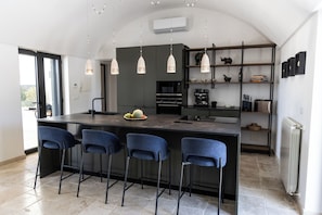 A modern kitchen with a central island, bar stools, pendant lighting, and a built-in oven. - Stunning Villa Teodoro (Ostuni)
