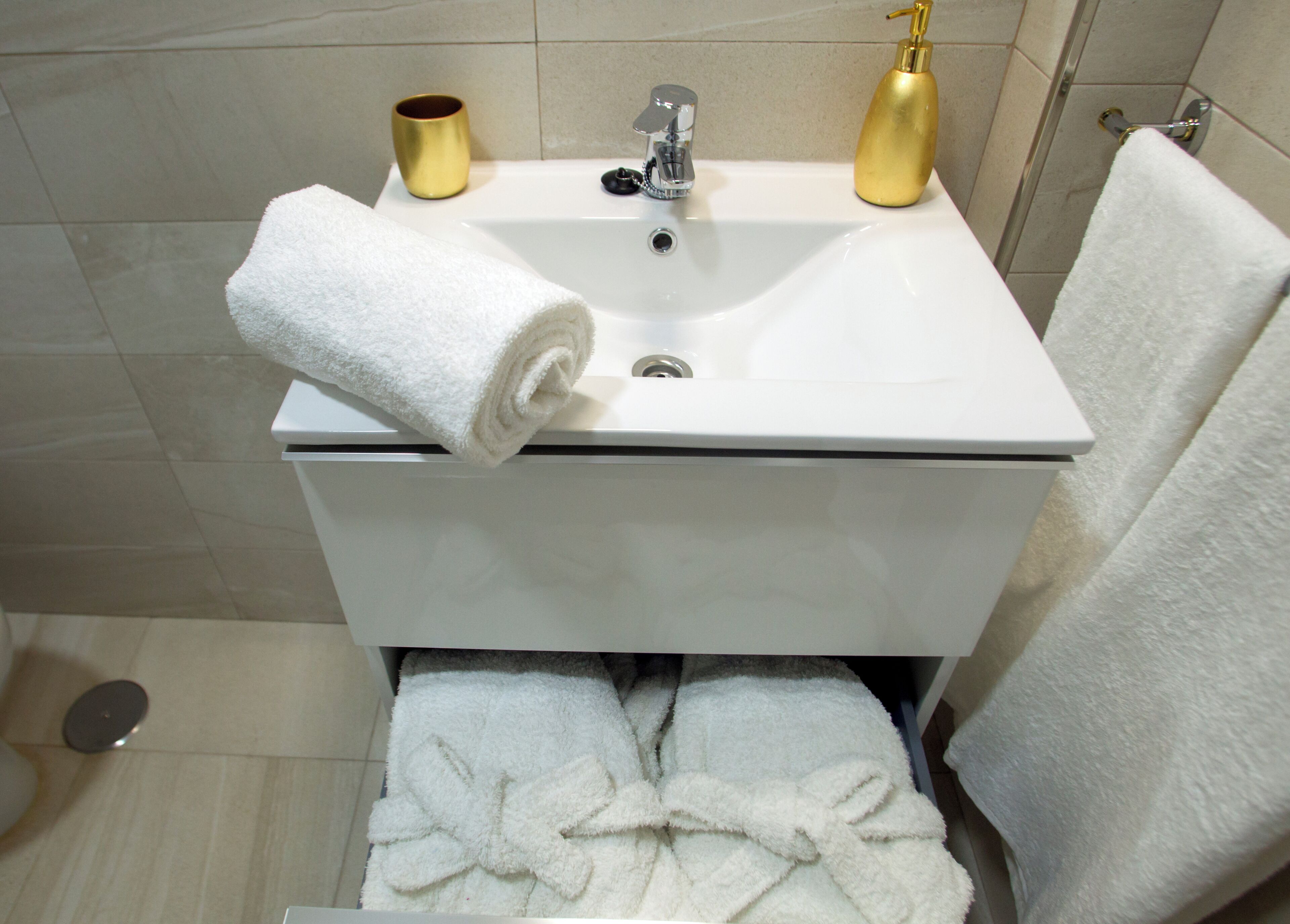 Een badkamer met een witte wastafel, gouden kraanwerk en een witte handdoek op het aanrecht.