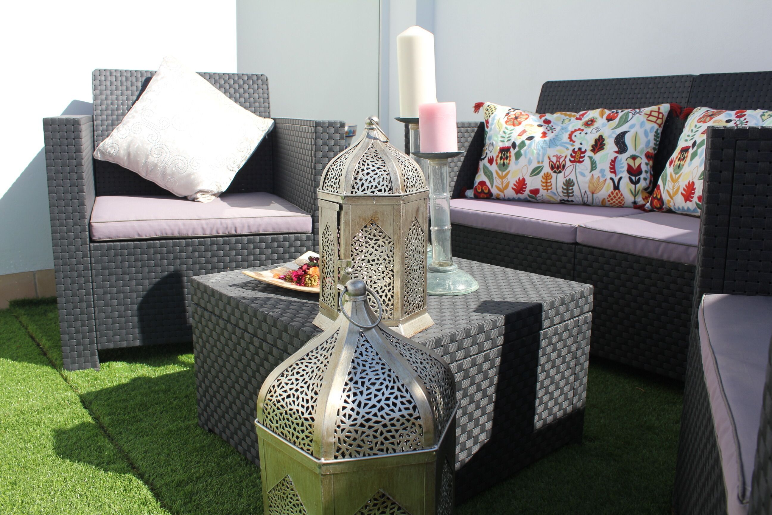Un espacio patio con mobiliario de mimbre, un farol decorativo y una vela sobre una mesa.