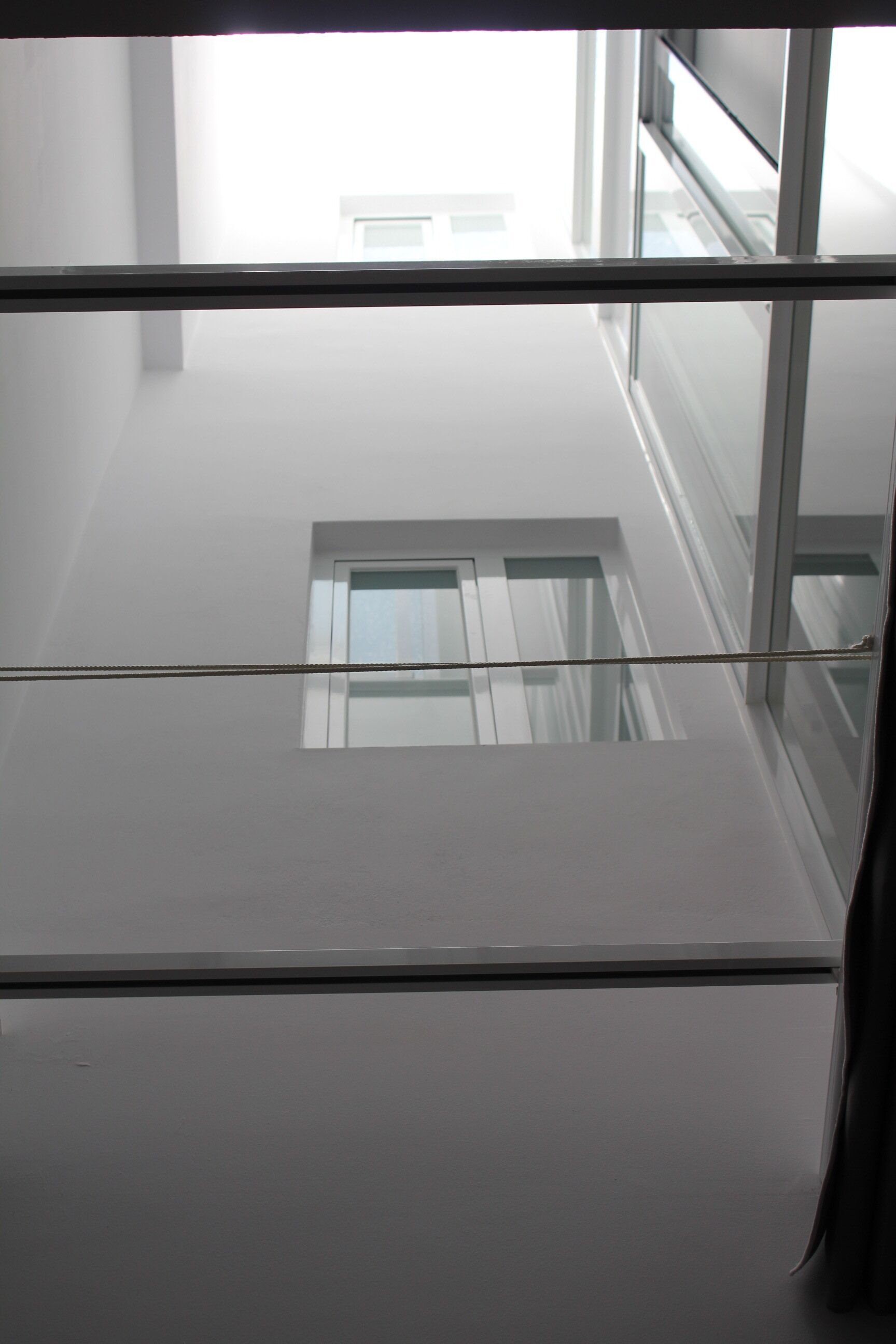 Une vue à travers une fenêtre, avec un ciel dégagé, un bâtiment doté d’un toit plat et une balustrade en verre.