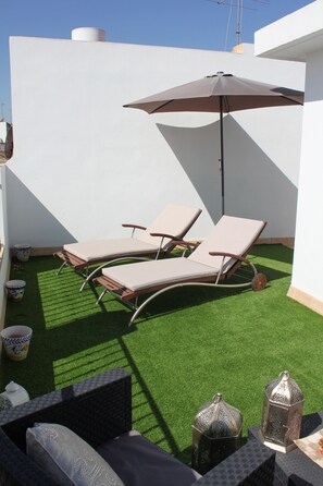 Una terraza en la azotea con dos sillones de descanso, un parasol grande y faroles decorativos.