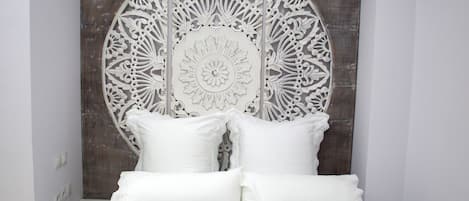 A bed with white bedding and decorative pillows, a bedside table with a remote control, and a wall with a circular decorative panel.