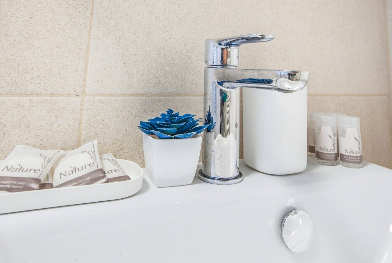 A bathroom sink with a chrome faucet, a white soap dispenser, and a soap dish with a blue decorative item.