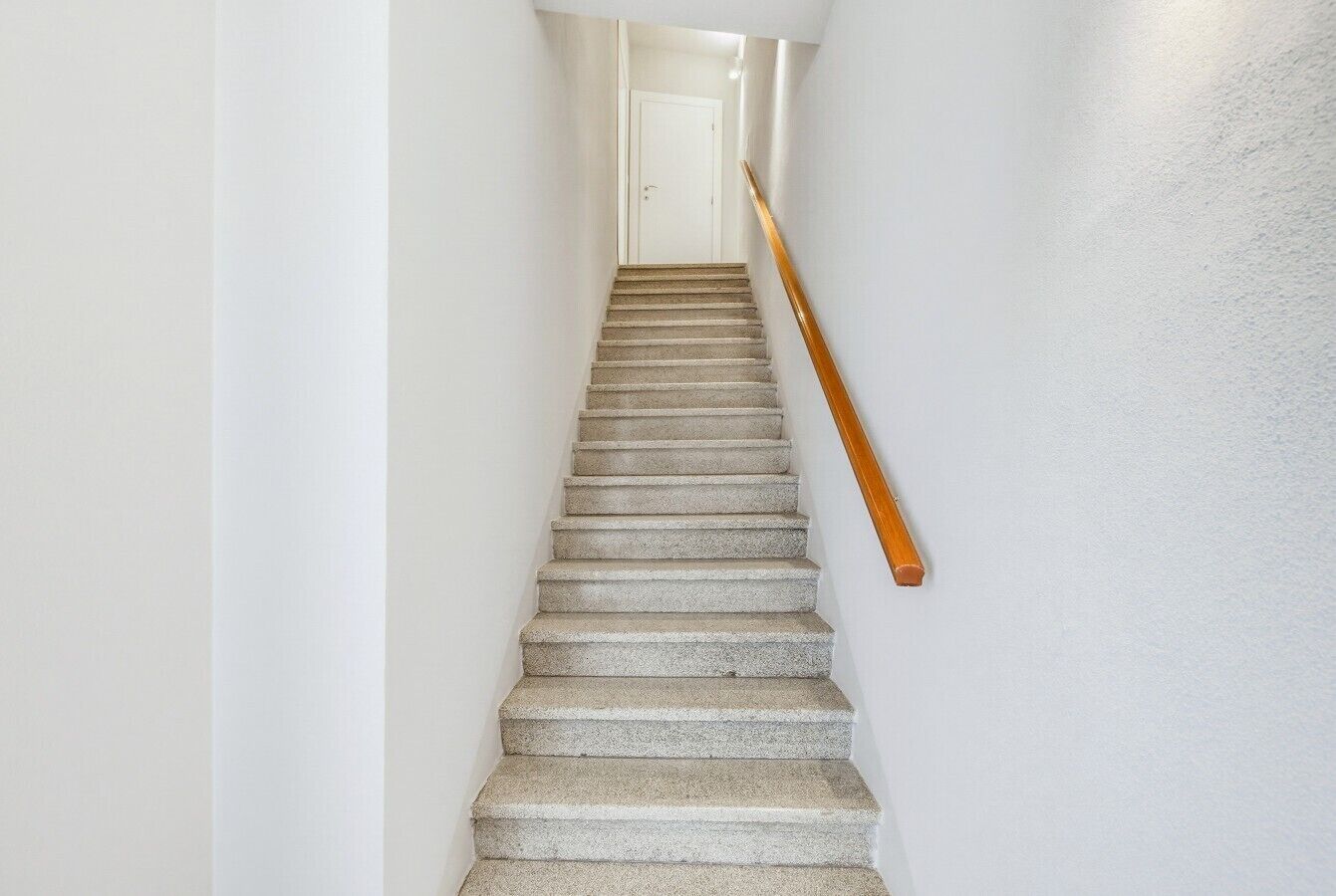 Una escalera con barandilla de madera que lleva a una puerta blanca al final.