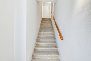 Eine Treppe mit einem hölzernen Geländer, das zu einer weißen Tür am oberen Ende führt.