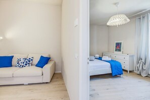 Ein Zimmer mit einer Couch, einem Bett, einer weißen Kommode, einer Pendelleuchte und einem gerahmten Bild an der Wand.