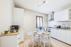 A modern kitchen with white cabinets, a dining table set for four, and a window with curtains. - Clara Olivi - Lavaiano (Lavaiano)