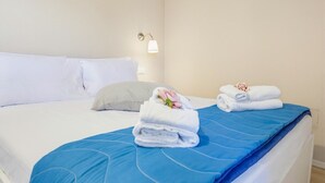Quarto de hotel com cama, almofadas, colcha azul e toalhas dobradas com flores.