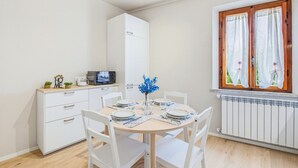 Uma cozinha compacta com micro-ondas, uma geladeira pequena e uma mesa de jantar posta para dois, com cadeiras.