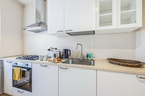 A modern kitchen with white cabinets, a stainless steel sink, a gas stove, a coffee maker, and a basket. - Clara Olivi - Lavaiano (Lavaiano)