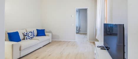 A modern living room with a sofa, a flat-screen TV, and a wooden floor.