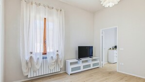 Um quarto com uma televisão sobre um suporte branco, um radiador branco e uma porta que dá para outro cômodo.