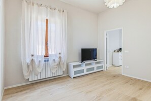 Ein Zimmer mit einem Fernseher auf einem weißen Schrank, einer weißen Heizung und einer Tür zu einem anderen Raum.