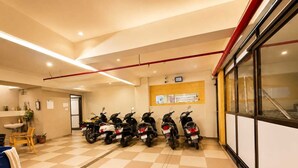 Un espacio interior limpio y bien iluminado con piso a cuadros, una fila de scooters estacionados, un lavamanos y una ventana con vistas.