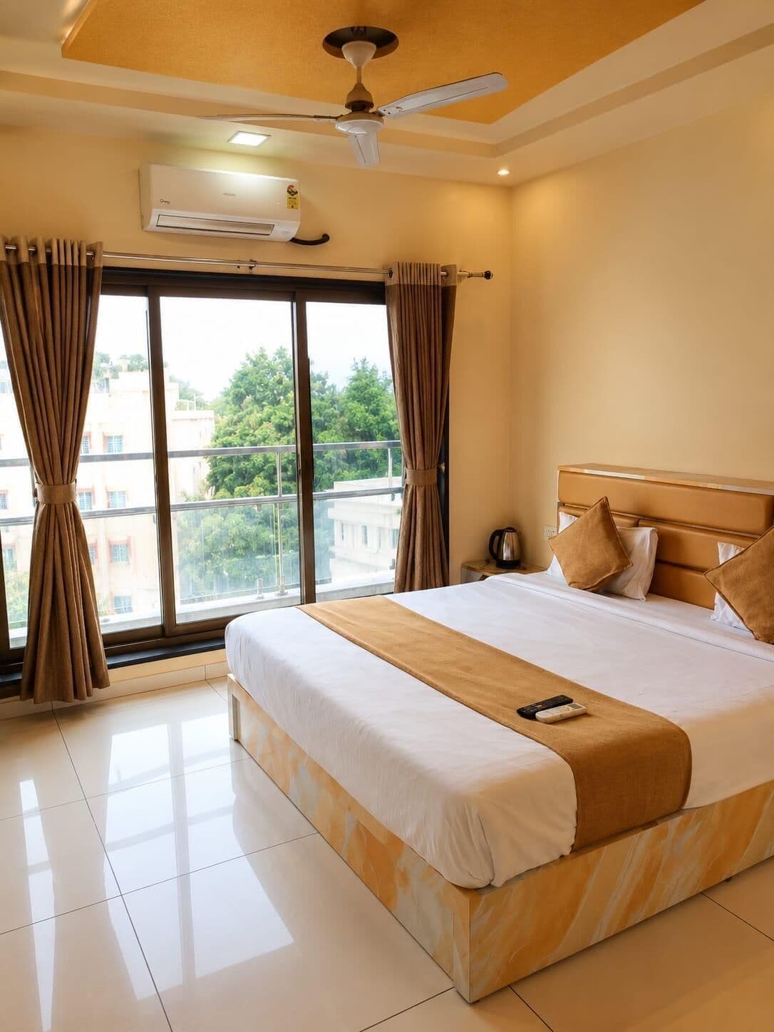 A hotel room with a large bed, a ceiling fan, an air conditioning unit, a nightstand, and a view of the outside.