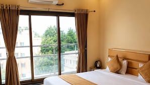 Habitación de hotel con una cama grande, ventilador de techo, equipo de aire acondicionado, mesita de noche y vista al exterior.