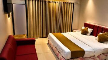 Una habitación de hotel con cama, un sofá rojo, televisión y una ventana con cortinas.