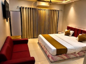 Una habitación de hotel con cama, un sofá rojo, televisión y una ventana con cortinas.