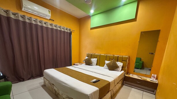 Una habitación de hotel con una cama, una silla verde, un espejo y un aire acondicionado instalado en la pared.