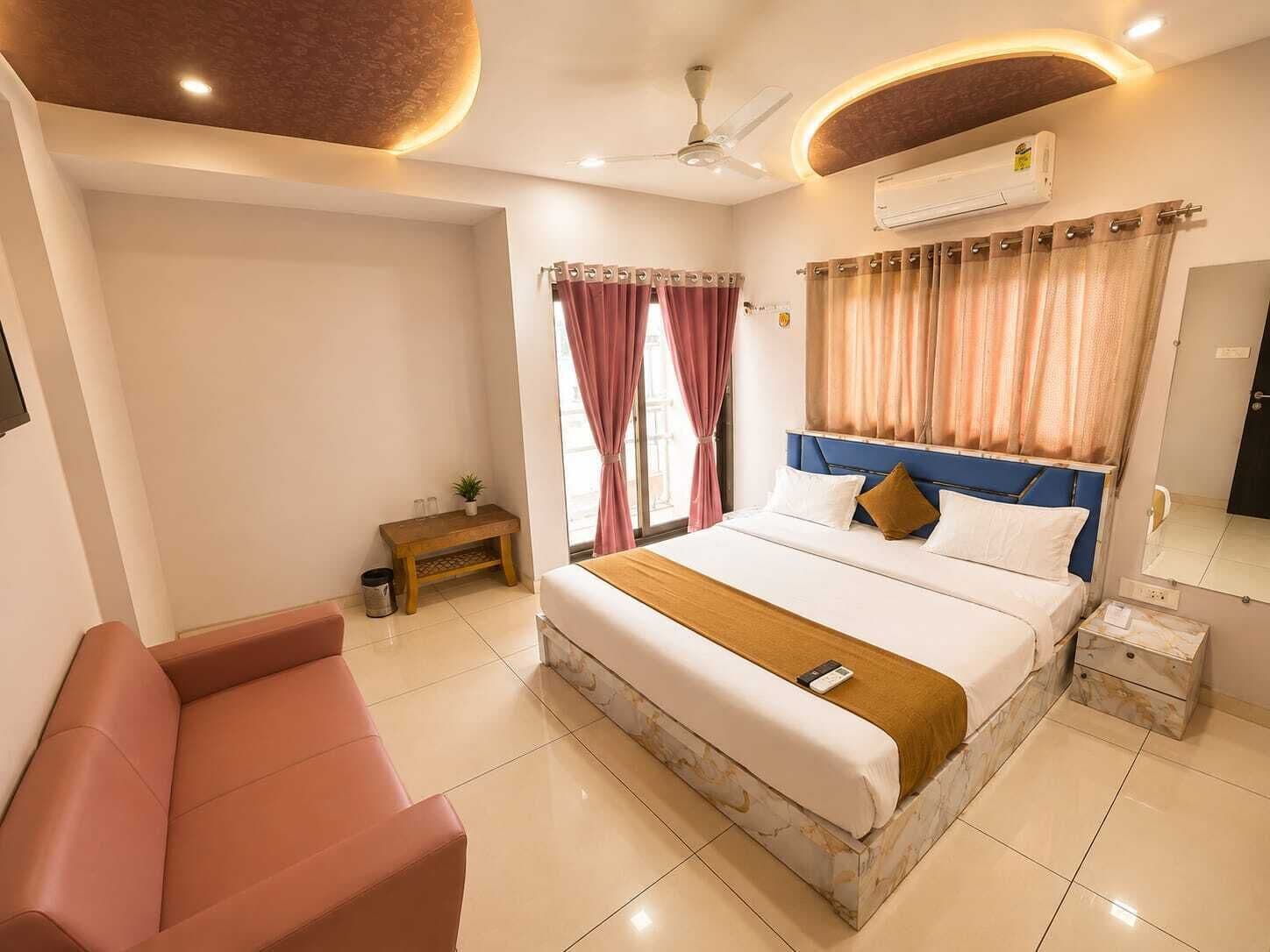 Une chambre d’hôtel comprenant un lit, une table de chevet, un petit banc, un canapé et un ventilateur de plafond.