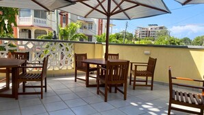 Un patio al aire libre con una mesa y sillas, un parasol grande y vistas de edificios al fondo.