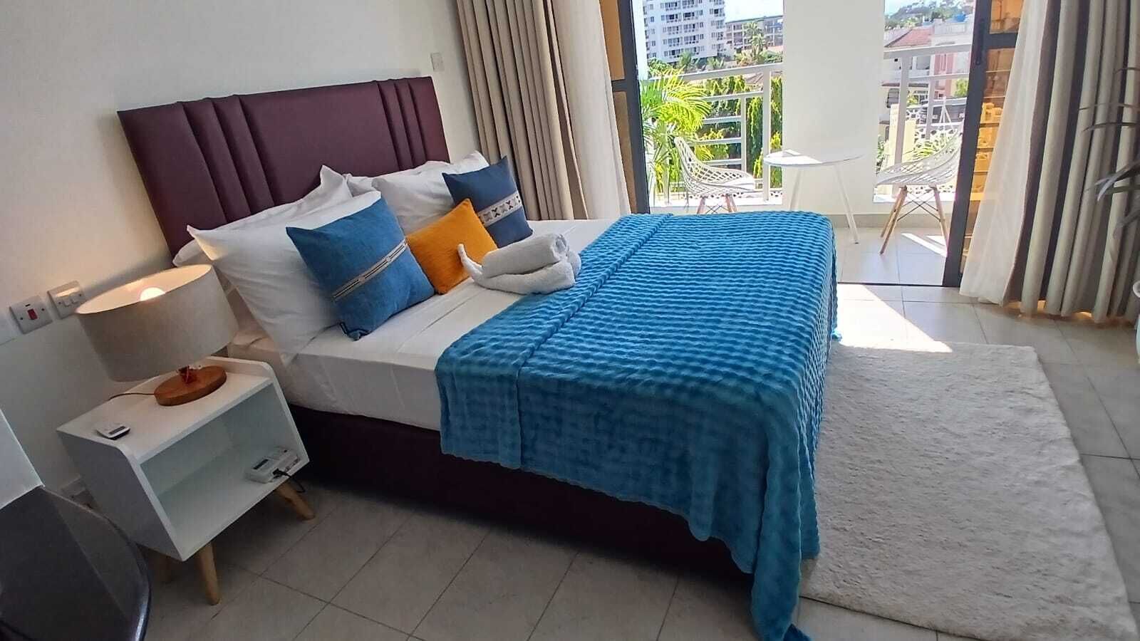 Una camera d'hotel con un letto, un comodino, una lampada e vista sul balcone.