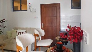 Un comedor con una mesa negra, cuatro sillas blancas y un florero con flores rojas.