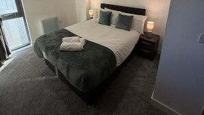 Ein Schlafzimmer mit einem Bett, einem Nachttisch, einer Lampe, einem Gemälde und einem Fenster mit Jalousien.