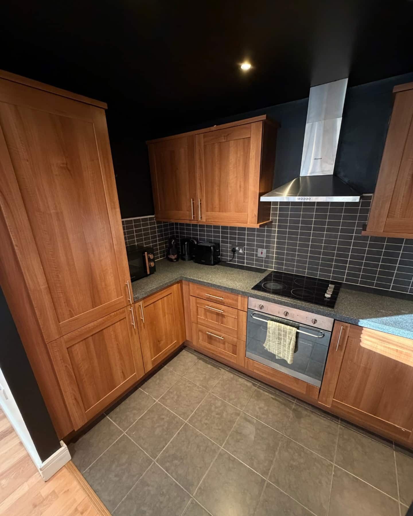 A kitchen with wooden cabinets, a black countertop, a stove, and a tiled backsplash.