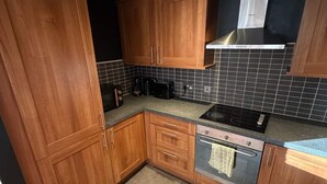 Eine Küche mit Holzschränken, einer schwarzen Arbeitsplatte, einem Herd und einer gefliesten Rückwand.