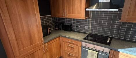 A kitchen with wooden cabinets, a black countertop, a stove, and a tiled backsplash.
