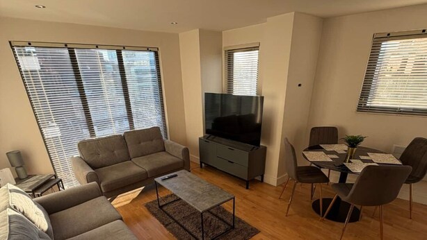 Ein modernes Wohnzimmer mit grauem Sofa, Couchtisch, Flachbildfernseher und Essbereich mit Tisch und Stühlen.
