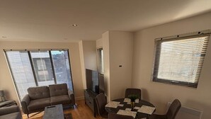 Ein modernes Wohnzimmer mit einer Couch, einem Couchtisch, einem Fernseher und einem Essbereich mit Stühlen und einem Tisch.