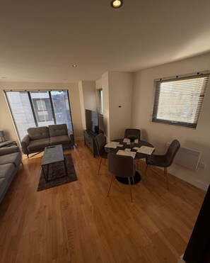 A modern living room with a sofa, coffee table, TV, and dining area with chairs and a table. - Elegant 2-Bed w/ Balcony | City Centre (Liverpool)