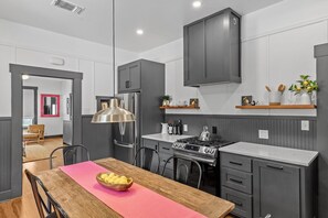 Een moderne keuken met grijze kastjes, een roestvrijstalen koelkast, een gasfornuis en een hanglamp.