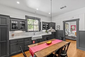 A modern kitchen with grey cabinets, a wooden dining table with a red table runner, and a window with a view of trees. - Prime Location | 5 Minute Walk to downtown+ Quiet Escape (Fredericksburg)